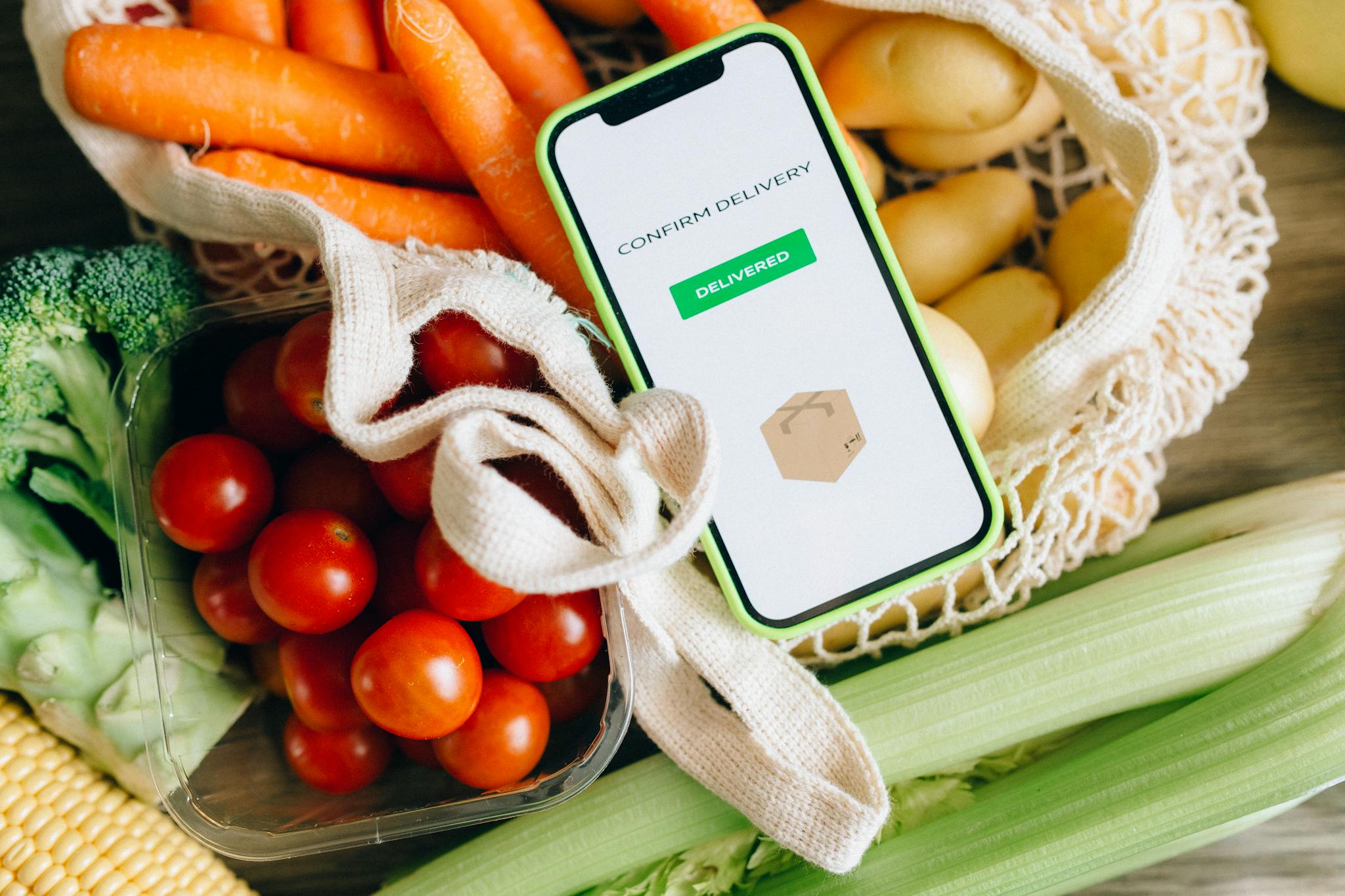 A smartphone displays delivery confirmation amidst fresh vegetables, signifying convenience and freshness.