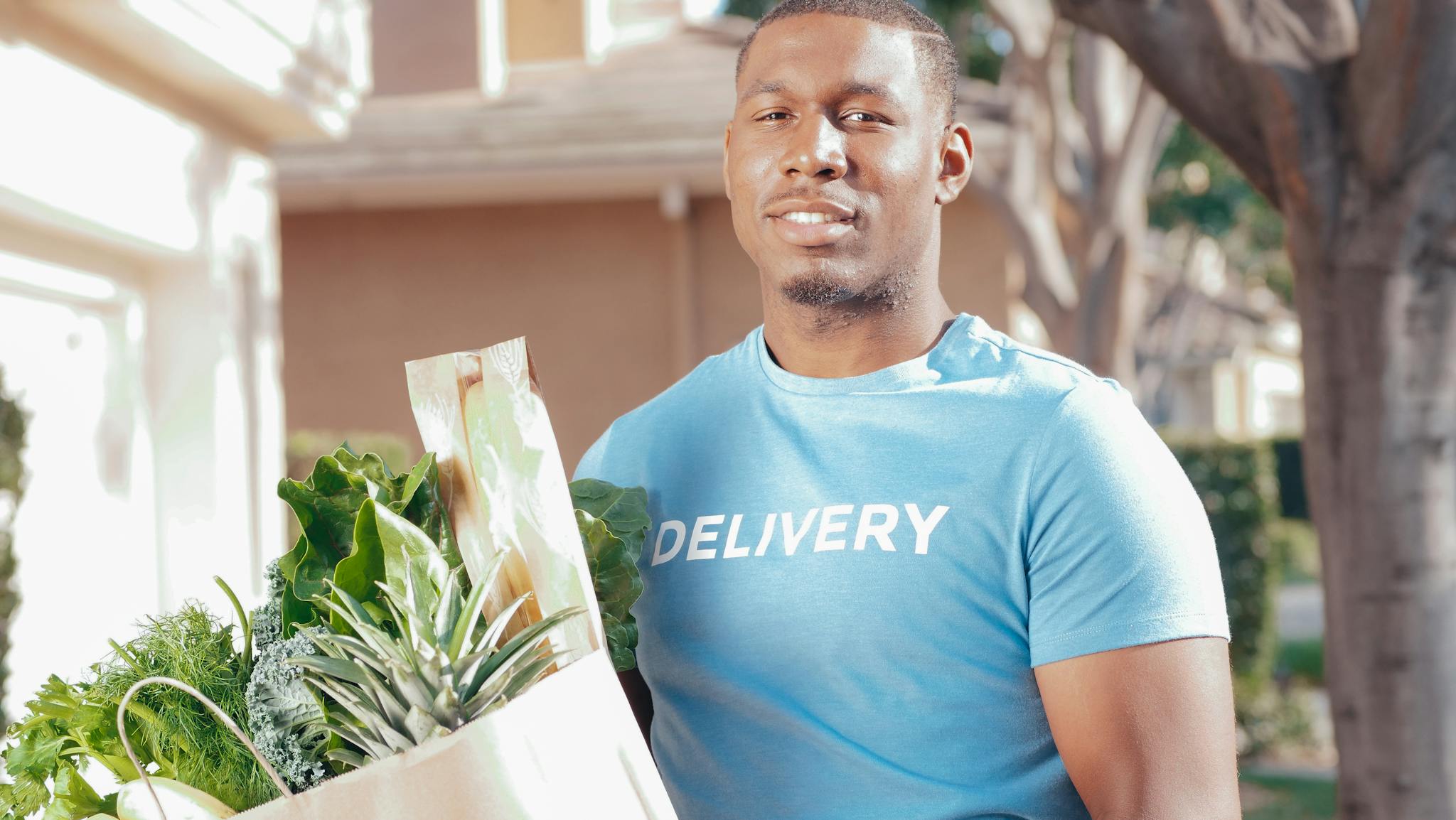 Smiling deliveryman holding a paper bag of fresh vegetables, providing excellent service outdoors.